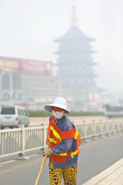近日，在古都洛陽，環(huán)衛(wèi)工人身后的“天堂”被霧霾籠罩著。