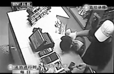 戴帽男子一手掐住加油站營(yíng)業(yè)員，一手持發(fā)令槍指向另一營(yíng)業(yè)員，要求“把錢給我裝起來(lái)”。