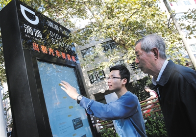 10月15日，滴滴工作人員（左）指導(dǎo)乘客使用“滴滴車站”的電子屏預(yù)約出租車。