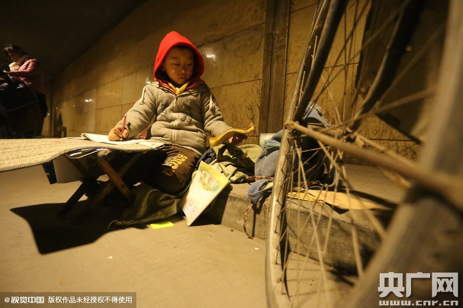 2015年11月8日晚，鄭州，7歲男孩涵洞橋下陪父母練攤，路邊燈下坐小馬扎上寫作業(yè)。