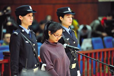 被告人盧梅低著頭，站在朝陽法院刑事審判庭的被告席上。